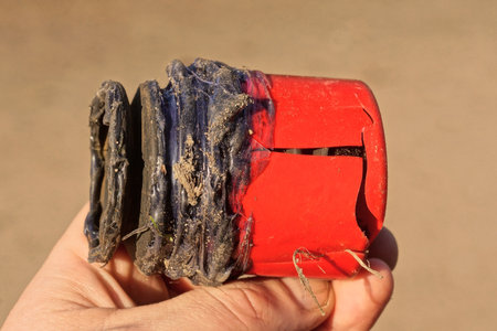 hand holding a piece of old black plastic plumbing pipe with a cracked red plug on a brown...
