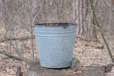 one old gray metal bucket stands on a wooden stump on the streetの写真素材