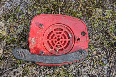 large broken headphones with one red plastic speaker and a black microphone lies on green moss and ground on the streetの写真素材