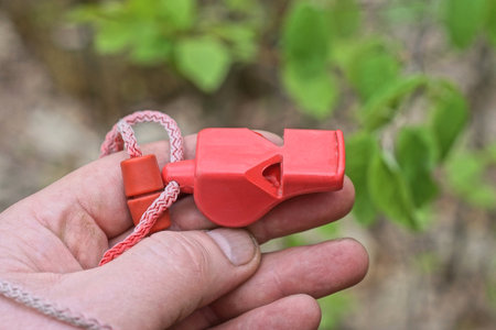 hand holding one red plastic whistle on a lanyard on the street