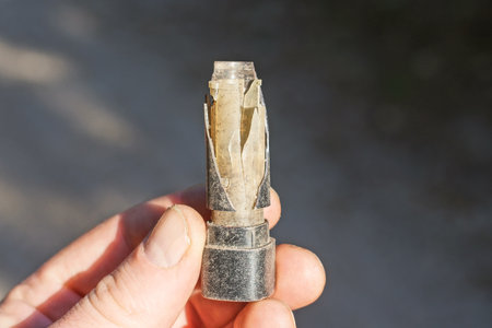 hand holding one broken old broken plastic empty white black lipstick bottle on the street on a gray...