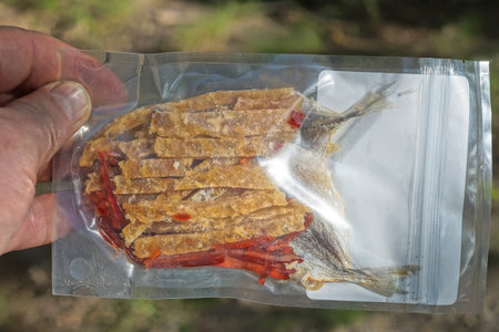 hand holds food set of small cut sea dry fish and dried squid in a transparent bag