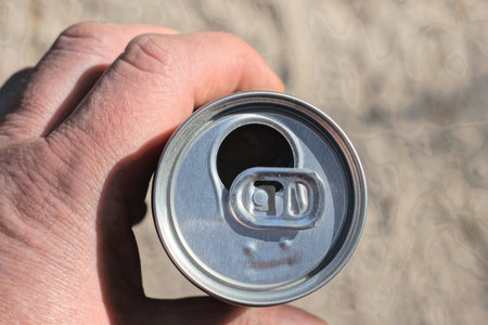 hand holding one white open aluminum can on the street on a gray background