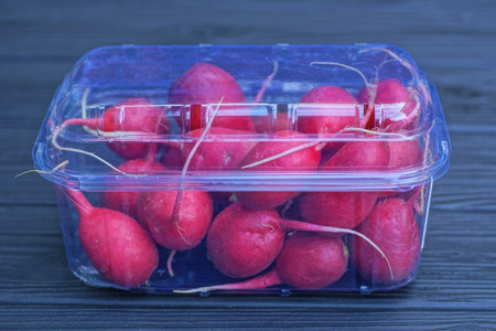 Red radish in plastic container on blue wooden table, closeupの写真素材
