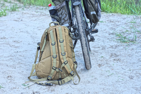 one brown backpack stands near a black bicycle on the gray sand outsideの写真素材