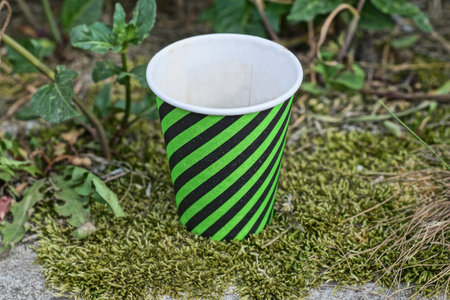 one paper striped cup of coffee stands on the gray ground near the green moss on the streetの写真素材