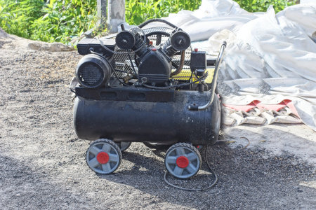 one black mobile generator compressor on wheels stands on the gray ground on the street