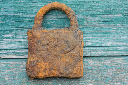 one big old brown rusty padlock stands against a green wooden wall on the streetの写真素材