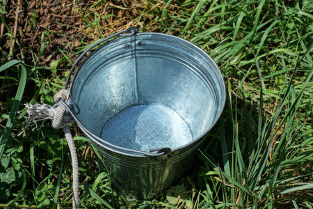 one gray large galvanized metal bucket with water stands outside in the green grass