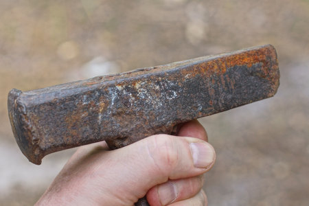 hand holding one brown old rusty iron hammer on street on gray background