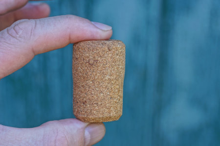 fingers holding one brown cork stopper on green backgroundの写真素材