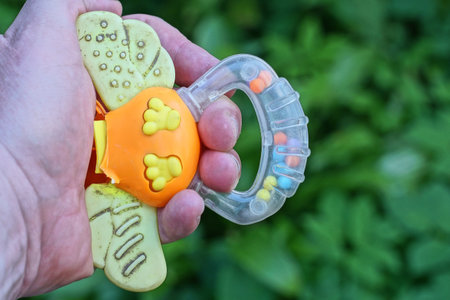colored plastic one toy rattle lies on the palm of the hand on the street