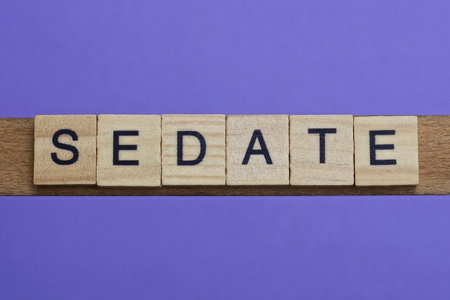 word sedate made from wooden gray letters lies on a lilac backgroundの写真素材