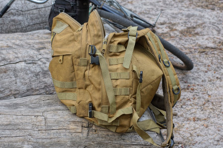 one brown army backpack stands on a gray wooden log on the street