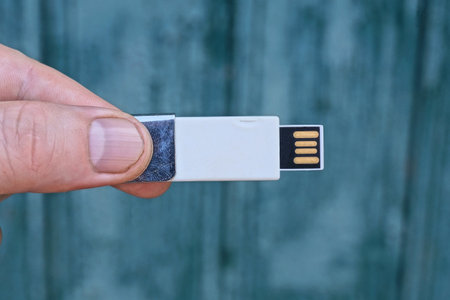 fingers on the hand hold one white small compact flash drive outdoors on a green background