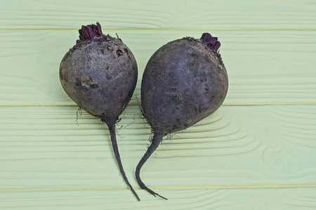 two gray raw beets lie on a yellow wooden table