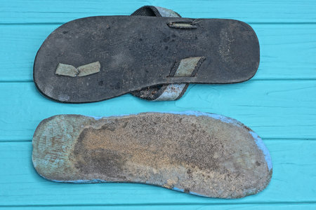 two old black gray dirty soles of slippers lie on a blue wooden tableの写真素材