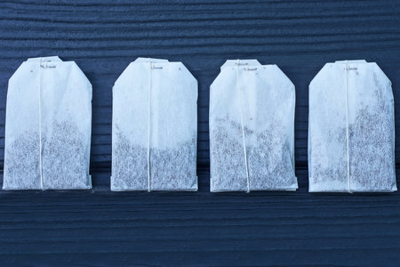 four white tea bags with black tea lie on a wooden tableの写真素材