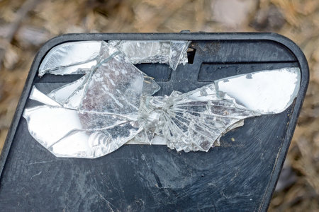 one black plastic mirror from car with white broken glass with cracks on brown background on street