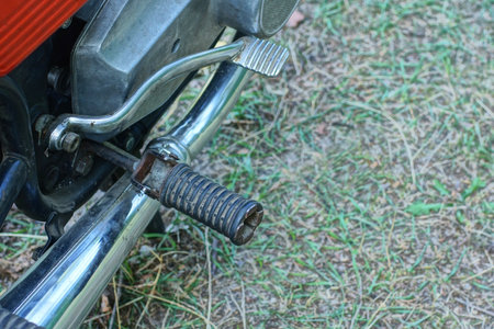 part of old motorcycle with gray iron starter leg above metal exhaust pipe on summer street above ground and green grassの写真素材