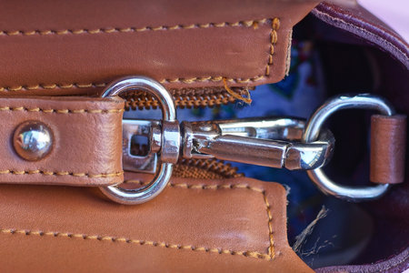 one white metal latch with a ring on the strap of a brown leather bagの写真素材