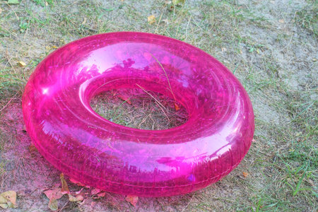 one plastic pink round inflatable swimming ring lies on the gray sand and green grass of a summer...