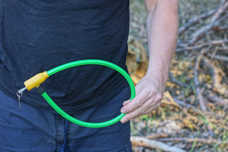 hand of a man in blue black clothes holds in his hand a yellow green long bicycle lock on a summer streetの写真素材