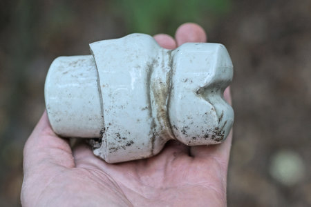 one old broken white dirty ceramic line insulator lies on the palm of the hand on the streetの写真素材