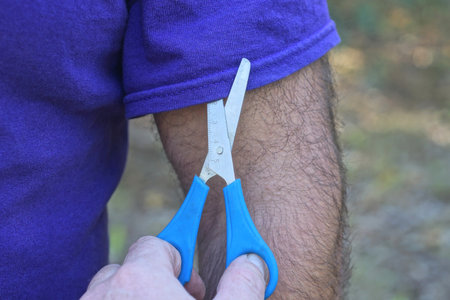 hands holding scissors cutting lilac sleeve from fabric shirt on manの写真素材
