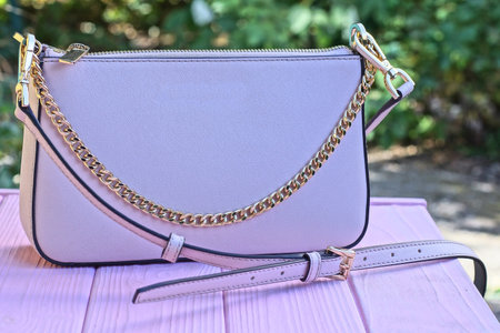 one pink leather bag with yellow chain and strap stands on wooden table on summer street against green vegetation backgroundの写真素材