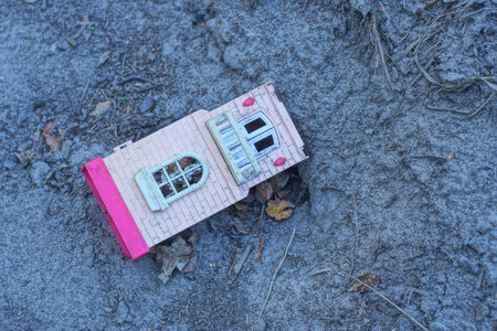 one pink white plastic house toy lies on gray sand in sandbox on summer playground
