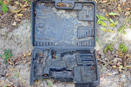 one old open broken dirty black plastic tool box lies on gray ground on summer streetの写真素材