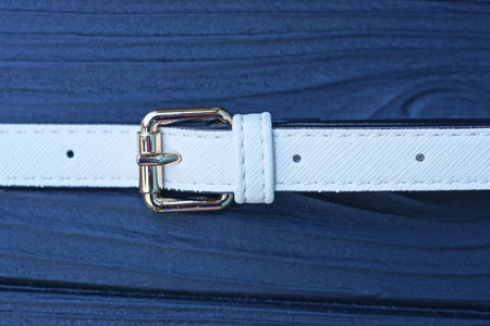one long leather white harness with a yellow metal clasp lies on a black wooden table