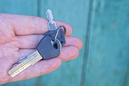fingers on the hand hold two door keys on a green background