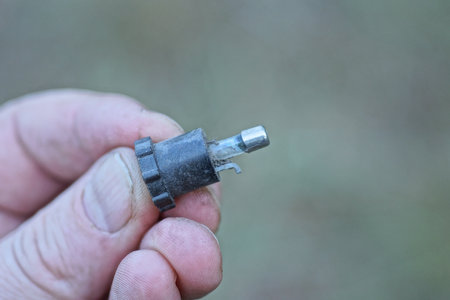 fingers of hand holding small gray glass old fuse in black boxの写真素材
