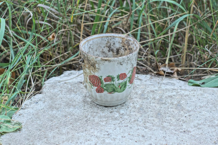 one dirty white broken cup with a colored pattern lies on the gray ground in the streetの写真素材