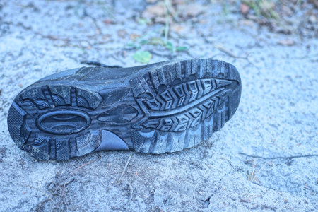 one old dirty leather black boot lies on the gray sand in the streetの写真素材