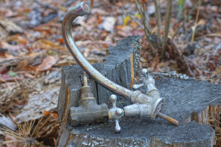 two old metal and brass water taps lie on a gray wooden stump on a summer street