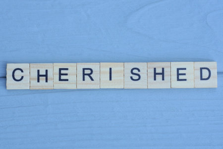 text the word cherished from wooden small letters with black font on an blue tableの写真素材