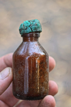 fingers holding one small brown medical glass bottle closed with a green cap on the streetの写真素材