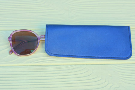 one brown plastic sunglasses lie in blue leather case on yellow wooden tableの写真素材