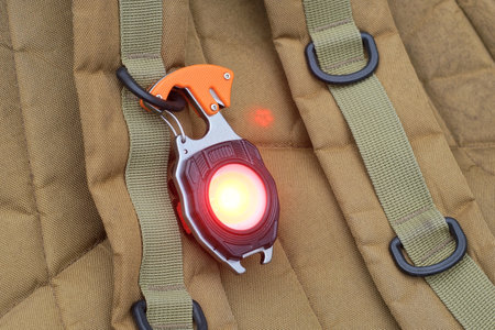 one small black flashlight with red light hangs on a brown backpack strap on a summer street