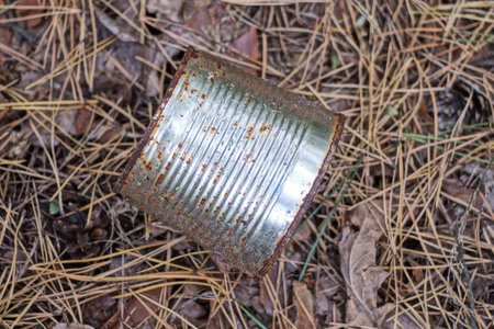 garbage from one white dirty metal tin can lies on brown ground in nature