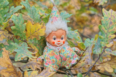 one little colorful clown toy sitting on a branch of an oak tree with green leaves in summer natureの写真素材