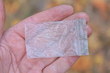 hand holding one small white plastic bag on a brown background on the streetの写真素材