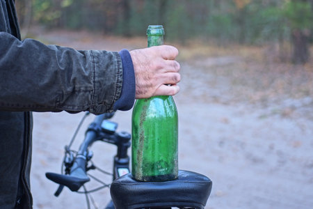 man holding big green empty glass bottle on black bicycle seat on autumn streetの写真素材