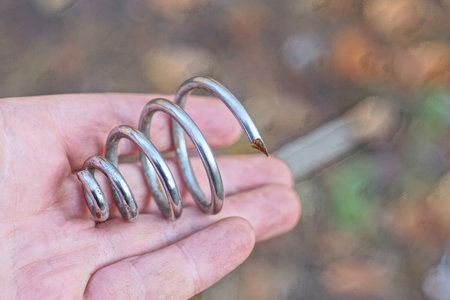 one old white iron spring from a bicycle seat lies on the palm of the hand on a summer street