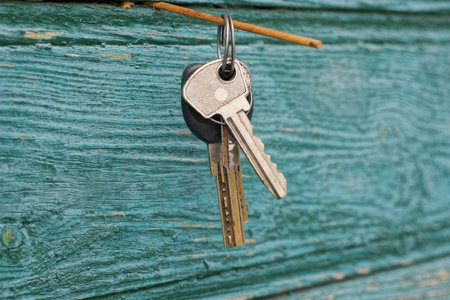 set of two metal door keys on iron ring hanging on green wooden wallの写真素材