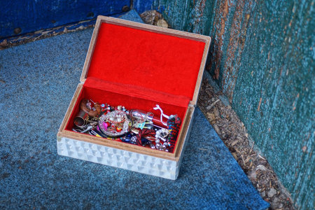 colorful jewelry and costume jewelry lie in a red white open box stands on a blue table near a green wallの写真素材