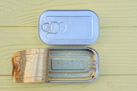 two open and closed gray metal tin cans stand on yellow wooden table